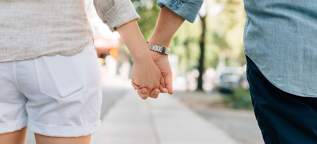 A man and a woman holding hands walking down the road